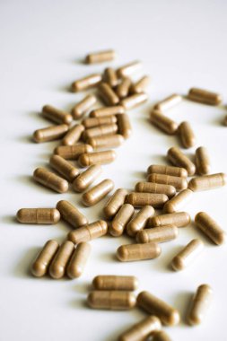 Kahverengi bitkisel kapsüllerin yakın plan çekimleri beyaz yüzeye yayılarak organik besinler, doğal tıp, sağlık terapisi ve bütünsel sağlık yaklaşımını temsil etmektedir..