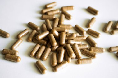 Kahverengi bitkisel kapsüllerin yakın plan çekimleri beyaz yüzeye yayılarak organik besinler, doğal tıp, sağlık terapisi ve bütünsel sağlık yaklaşımını temsil etmektedir..