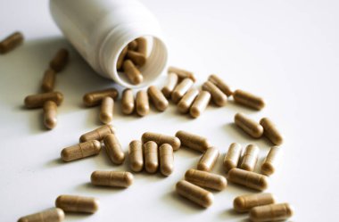 Kahverengi bitkisel kapsüllerin yakın plan çekimleri beyaz yüzeye yayılarak organik besinler, doğal tıp, sağlık terapisi ve bütünsel sağlık yaklaşımını temsil etmektedir..