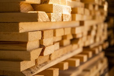 Güneş ışığının yaktığı pürüzlü kenarları olan istiflenmiş kerestelerin yan görünüşü, inşaat, marangozluk ve marangozluk için temel bir kaynak olarak doğal keresteyi sembolize ediyor..