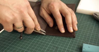 Close-up of craftsman hands carefully cutting leather on a green cutting mat. The process highlights precision, handmade craft, and traditional work.