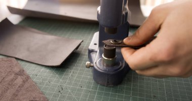 Craftsman hand installing metal snap button on leather piece with press tool during handmade leather goods production.