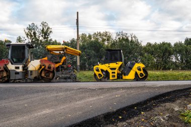 Multiple road rollers and paving machinery working on fresh asphalt during road construction. Heavy equipment compresses pavement for infrastructure projects.
