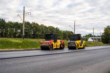 Two asphalt rollers, yellow and red, working side by side on a road construction site. Heavy machinery compresses new pavement for infrastructure development.