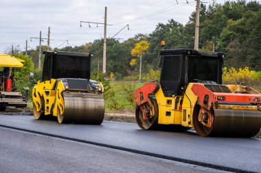Two road rollers compressing newly laid asphalt on a road construction site. Heavy machinery ensures strong pavement for modern infrastructure development.