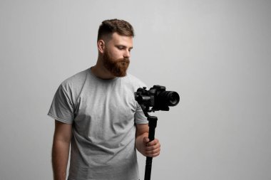 Male videographer with beard holding professional camera on stabilizer. Concept of filmmaking, video production, creativity, technology, content creation, and lifestyle.