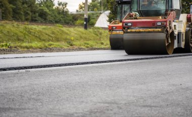 Heavy road rollers compacting fresh asphalt layer on road. Concept of infrastructure, civil engineering, road maintenance, road building, and construction machinery.