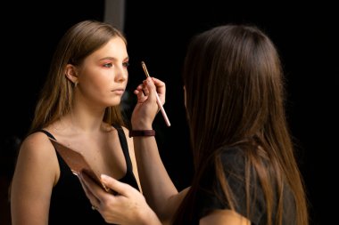 Profesyonel makyöz stüdyoda genç bir kadına göz farı sürüyor. Güzellik, kozmetik, moda, cazibe ve profesyonel bakım kavramı.