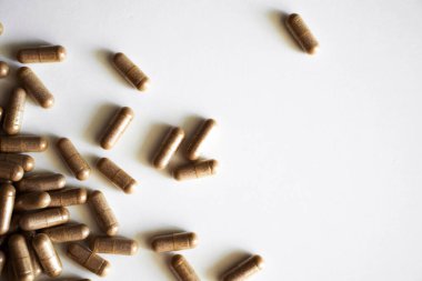 Beyaz yüzeye saçılmış kahverengi bitkisel destek kapsüllerinin yakın çekimi. İlaç, sağlık, doğal beslenme, eczane ve alternatif terapi kavramı.