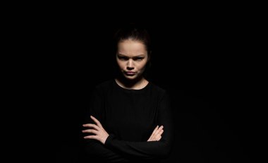 Kızgın yüz ifadesi ve çapraz kolları olan genç bir kadının stüdyo portresi. Duygu, psikoloji, olumsuz ruh hali, tutum, güç ve güven kavramı.