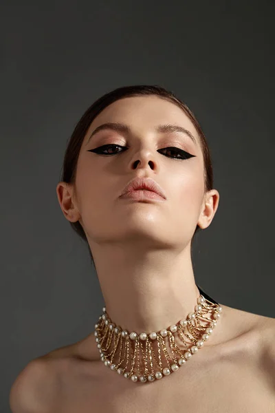 Genç moda model şık makyaj ve gri arka plan üzerinde poz altın kolye ile güzellik portresi.