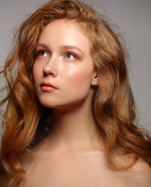 güzel genç kadının çıplak makyaj ve uzak gri arka plan üzerinde poz uzun kıvırcık saç seyir stüdyo portre