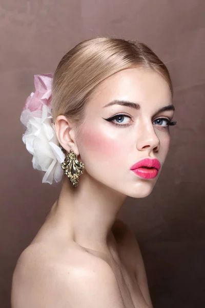 Fashion portrait of young blonde model with pink lips and roses in her hair wearing vintage earrings