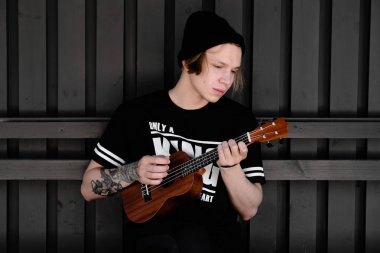 Akustik gitar veya ukulele açık oynayan genç adam