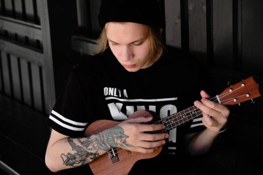 Akustik gitar veya ukulele açık oynayan genç adam
