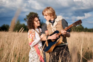 Boho stil çekici çift sonbahar sahada poz seviyorum. Aile eğleniyor ve gülüyor, oyun gitar. Çingene tarzı kıyafetler. Genç sarışın erkek ve beyaz kadın birlikte güzel açık.