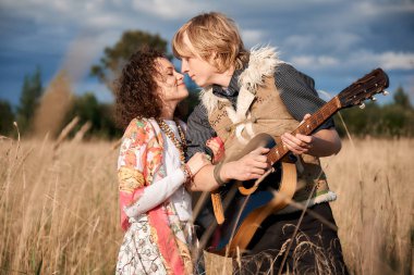 Boho stil çekici çift sonbahar sahada poz seviyorum. Aile eğleniyor ve gülüyor, oyun gitar. Çingene tarzı kıyafetler. Genç sarışın erkek ve beyaz kadın birlikte güzel açık.