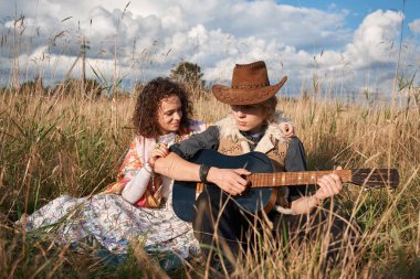 Boho stil çekici çift sonbahar sahada poz seviyorum. Aile eğleniyor ve gülüyor, oyun gitar. Çingene tarzı kıyafetler. Genç sarışın erkek ve beyaz kadın birlikte güzel açık.