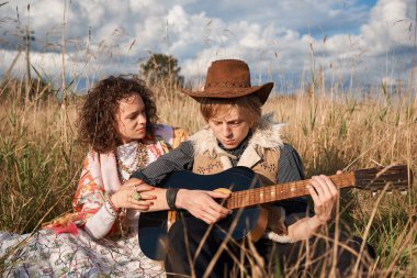 Boho stil çekici çift sonbahar sahada poz seviyorum. Aile eğleniyor ve gülüyor, oyun gitar. Çingene tarzı kıyafetler. Genç sarışın erkek ve beyaz kadın birlikte güzel açık.
