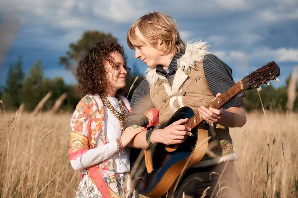 Boho style attractive couple in love posing on the autumn field. Family having fun and laughing, play guitar.  Gypsy style clothes. Young blonde man and beautiful caucasian woman together outdoor.