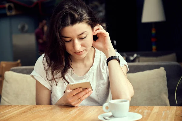 Mladá Žena Sedí Kavárně Dřevěného Stolu Pití Kávy Pomocí Smartphonu — Stock fotografie