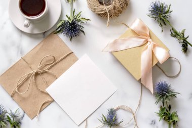 Kahve, mavi çiçekler, kartpostal, kraft zarf, sicim, pamuk şube, Hediyelik, Davetiyeli kopya alanı metin için fincan ile mermer masası. Düz yatıyordu, en iyi görünüm. Kadının gün veya annenin gün mockup.
