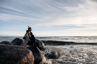 Şehvetli kaç içinde taşlar okyanus, sarılma ve konuşurken, rahatlatıcı yakınındaki plajda oturup seviyorum, günbatımı keyfini çıkarın