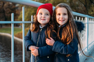 İki mutlu çocuk sonbahar parkta sarılma. Güneşli yaşam tarzı moda portre sevimli trendy kıyafeti giymiş iki güzel beyaz kız açık havada, kapatın. Little sisters gülüyor, rahatlatıcı, hayattan zevk