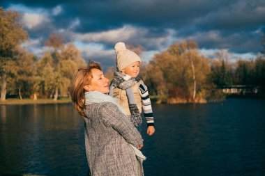 Anne ve oğlu sonbahar park. Mutlu aile açık havada, günbatımı üzerinde anne sarılma genç çocuk. Portre kadar kapatın.