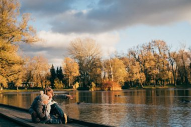 Anne ve oğlu yakın göl Sonbahar Park günbatımı üzerinde oturan ve uzağa arıyorsunuz. Eğlenceli, sarılma, gülen, rahatlatıcı, sahip aile yaşam keyfini çıkarın. Mutlu şık aile güneşli yaşam tarzı moda portre kadar kapatın