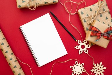 Noel hazırlık sunar. Defter, kalem, Kraft kağıt, dekoratif kar taneleri, Paketli hediyeler sicim kırmızı zemin üzerine. Noel ve mutlu yeni yıl kompozisyon. Yat style, üstten görünüm, tepegöz, alanı Kopyala