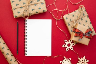Noel hazırlık sunar. Defter, kalem, Kraft kağıt, dekoratif kar taneleri, Paketli hediyeler sicim kırmızı zemin üzerine. Noel ve mutlu yeni yıl kompozisyon. Yat style, üstten görünüm, tepegöz, alanı Kopyala