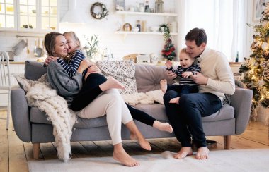 Mutlu bir aile yatak odasında eğleniyor. Neşeli genç aile kucaklayan gülen ve evde kanepenin üstüne oturan çocuklar ile