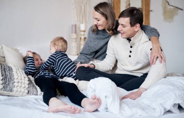 Mutlu bir aile yatak odasında eğleniyor. Kucaklayan ve yatakta gülüyor çocuklarla neşeli genç Aile.