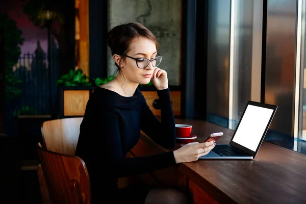 Joven Mujer Bonita Gafas Trabaja Ordenador Portátil Utiliza Teléfono Inteligente —  Fotos de Stock