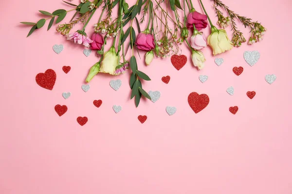 Valentines day composition : flowers and heart shaped valentines card confetti lay on top border on pink background. Love concept. Flat lay, top view, copy space.