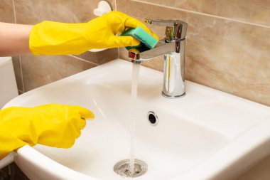 Lavabo, hizmet anlayışı temizlik temizlik. El kadının eller sarı beyaz seramik üzerinde koruyucu lastik eldiven paslanmaz çelikten akan suyun altında yeşil sünger ile dokunun Havzası.