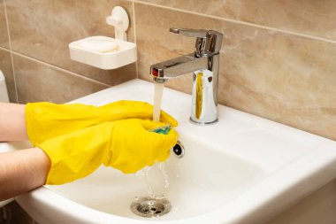 Lavabo, hizmet anlayışı temizlik temizlik. El kadının eller sarı beyaz seramik üzerinde koruyucu lastik eldiven paslanmaz çelikten akan suyun altında yeşil sünger ile dokunun Havzası.