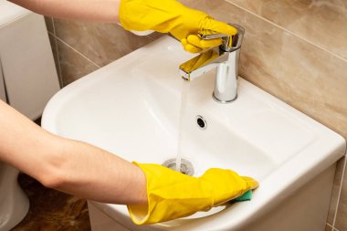 Lavabo, hizmet anlayışı temizlik temizlik. El kadının eller sarı beyaz seramik üzerinde koruyucu lastik eldiven paslanmaz çelikten akan suyun altında yeşil sünger ile dokunun Havzası.