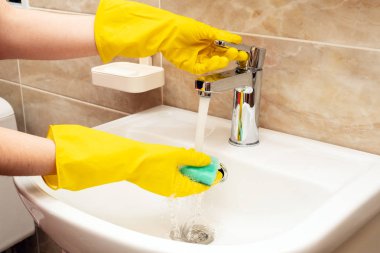 Lavabo, hizmet anlayışı temizlik temizlik. El kadının eller sarı beyaz seramik üzerinde koruyucu lastik eldiven paslanmaz çelikten akan suyun altında yeşil sünger ile dokunun Havzası.