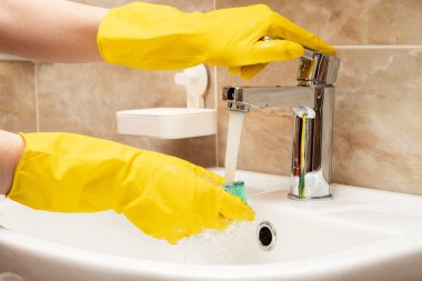 Lavabo, hizmet anlayışı temizlik temizlik. El kadının eller sarı beyaz seramik üzerinde koruyucu lastik eldiven paslanmaz çelikten akan suyun altında yeşil sünger ile dokunun Havzası.