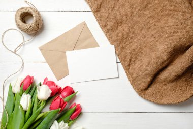 Lale çiçek, kraft zarf, sicim, çuval bezi Beyaz ahşap masa üzerinde buket. Vintage tebrik kartı womans günü, anneler günü, doğum günü, Paskalya için. Rustik arka plan, düz lay, görünümü.
