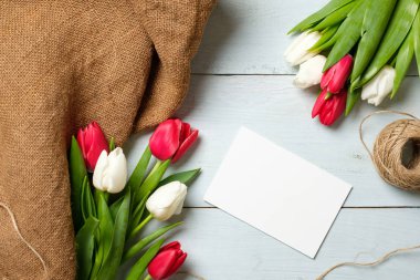 Demet lale, çuval bezi kumaş ve ışık mavi ahşap masa kartında boş kağıt. Paskalya, kadının günü, anneler günü, Bahar tatili için afiş mockup