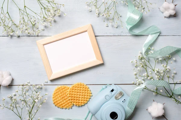 Womens desk with photo camera, picture frame, cookies. Spring minimal flowers frame, pastel colors, flat lay style, top view. Beauty technology concept, fashion blogger photo device.