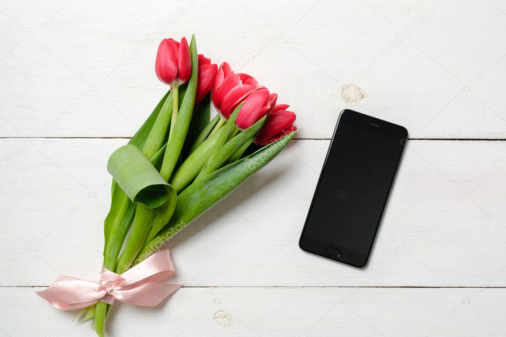 Conceptual composition of online dating app or site, tulip bouquets and mobile phone on white wooden background, romantic dating card, love card with spring flowers