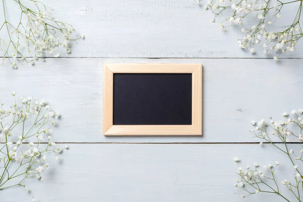 Framework for photo or congratulation on blue rustic wooden desk with flowers. Spring background, banner mockup for Womens or Mothers Day, Easter, spring holidays. Flat lay, above view.