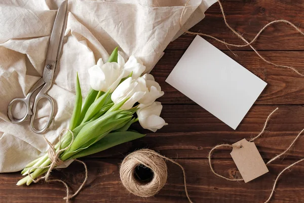 Beyaz Lale çiçek, boş kağıt kartı, makas buket Bahar, rustik ahşap masanın üstünde sicim. Kadın gün Bileşim görünümünün üzerinde düz yatıyordu stili.