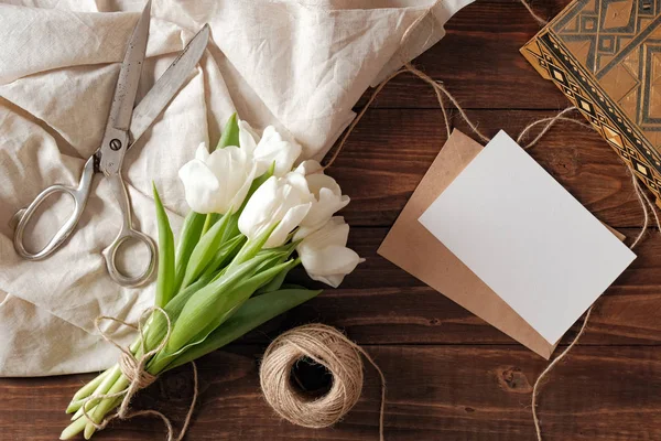 Beyaz Lale çiçek, kraft zarf boş kart, makas ile buket Bahar, rustik ahşap masaya sicim. Düğün günü kompozisyon görünümünün üzerinde düz yatıyordu stili.