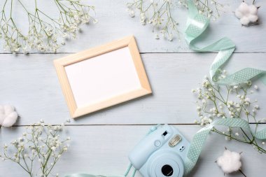 Fotoğraf çerçevesi mavi ahşap masa üzerinde kamera ve resim. En az çiçekli çerçeve, pastel renkler Bahar, düz stil, üstten görünüm yatıyordu. Güzellik teknoloji kavramı, moda blogger fotoğraf aygıt.