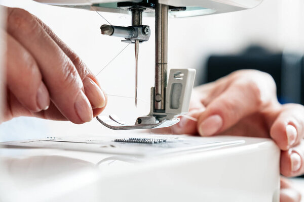 Женская рука держит нитку и нанизывает нитку на иглу швейной машинки
